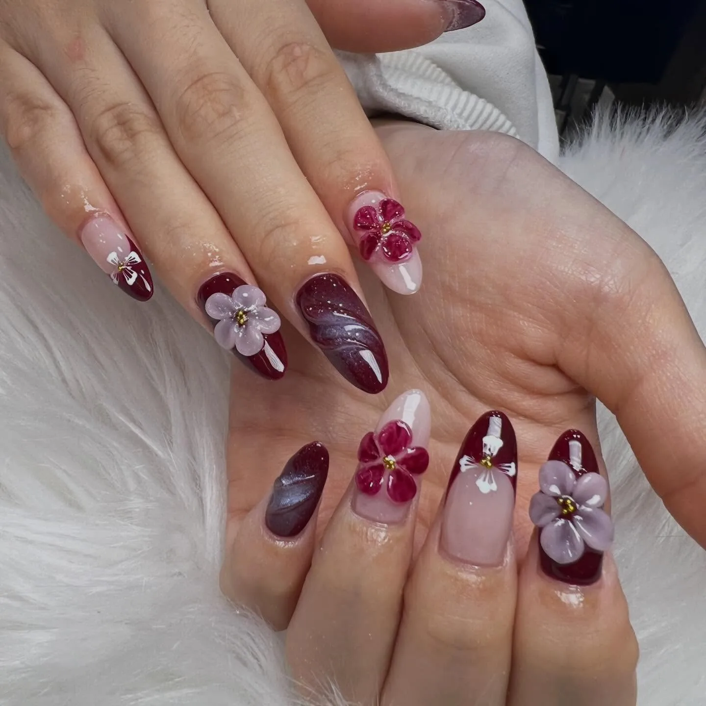 Deep burgundy almond nails with 3D lilac and magenta flowers, white fur