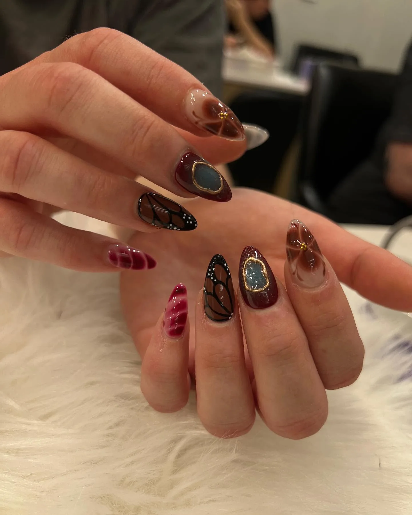 Burgundy and brown almonds with blue-stone gold bezel and black butterfly-wing art