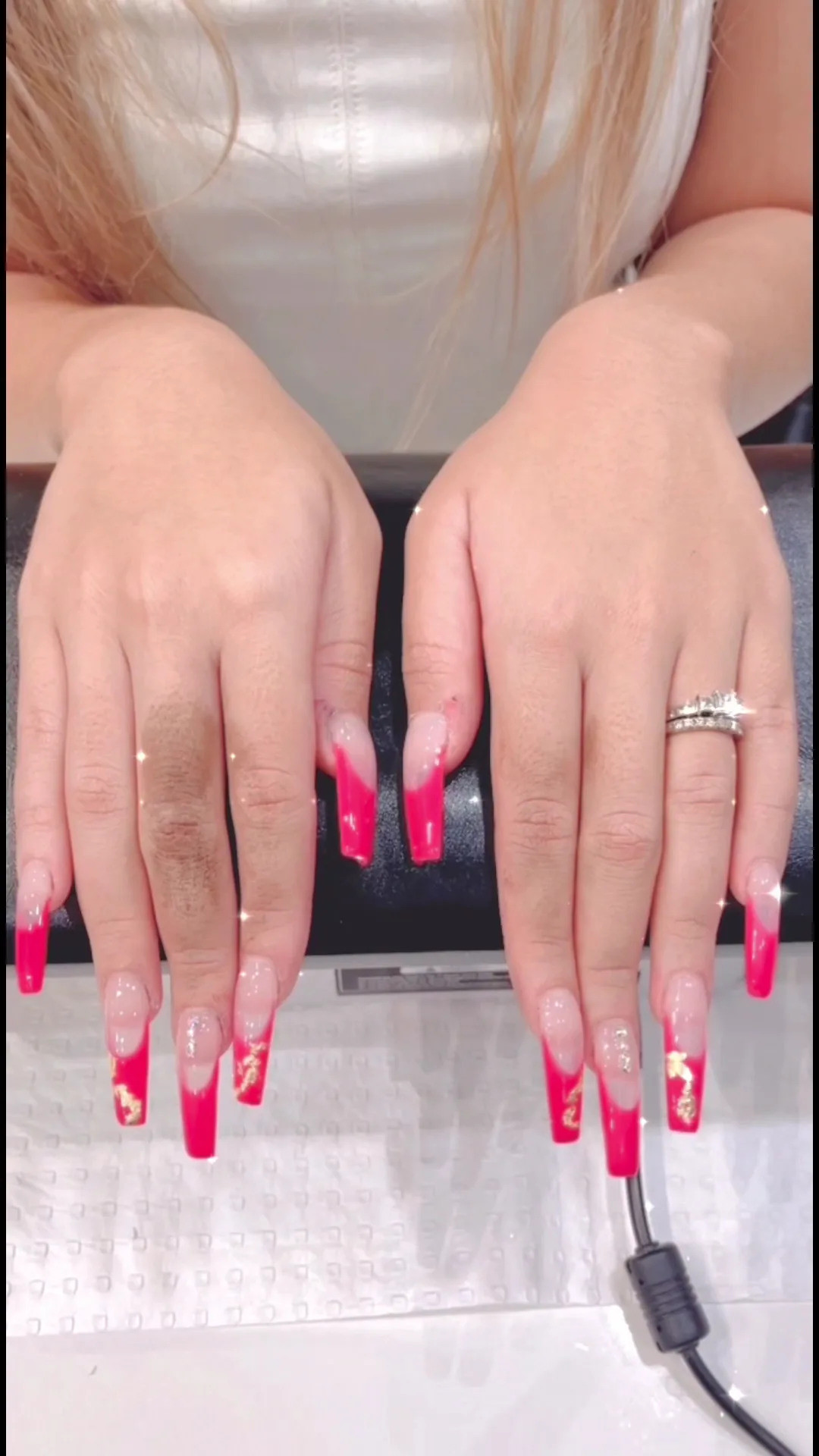Hot-pink long square nails with gold foil under a nail lamp